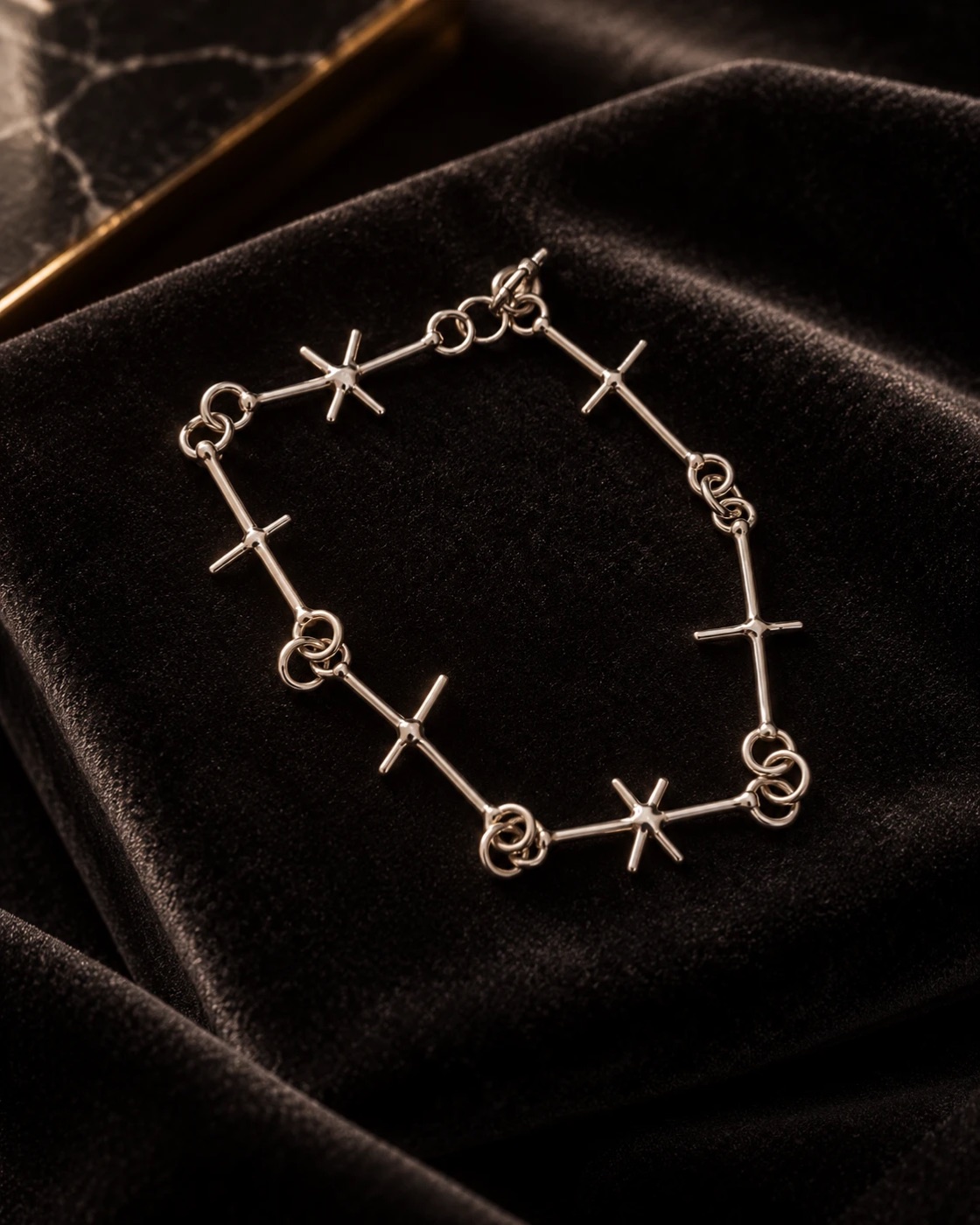 Silver bracelet made of straight bar links with cross and star shaped junctions, joined by rings, laid on black velvet
