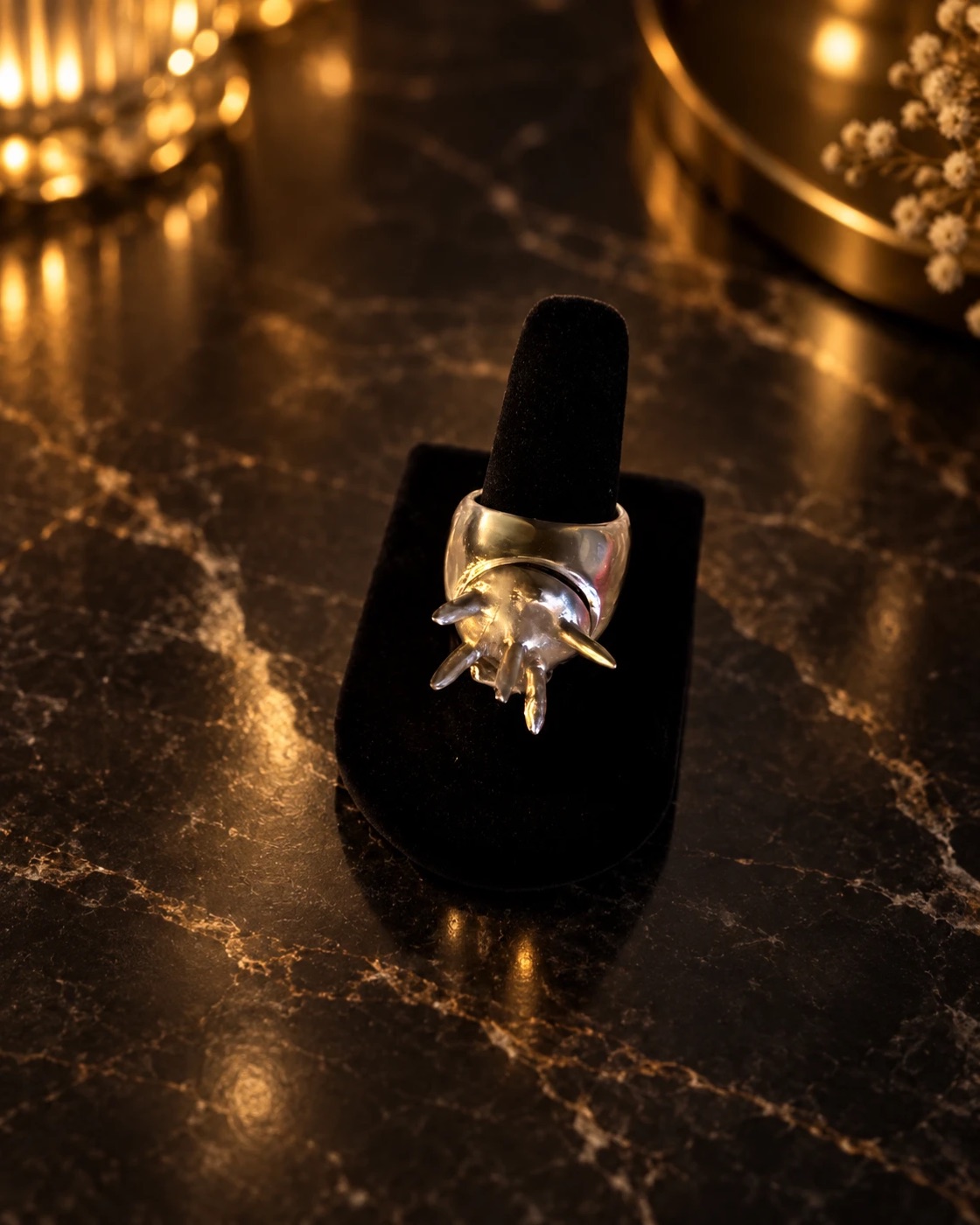 Polished silver ring with a spiked dome, closed, on a black velvet stand over dark marble